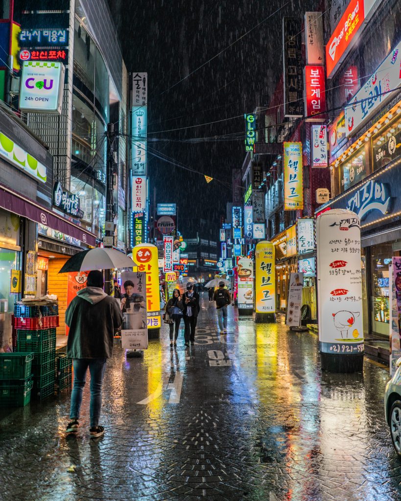 A picture of Korean street at night with lots of lighted signs, representing the sentence, I will have been living in Korea