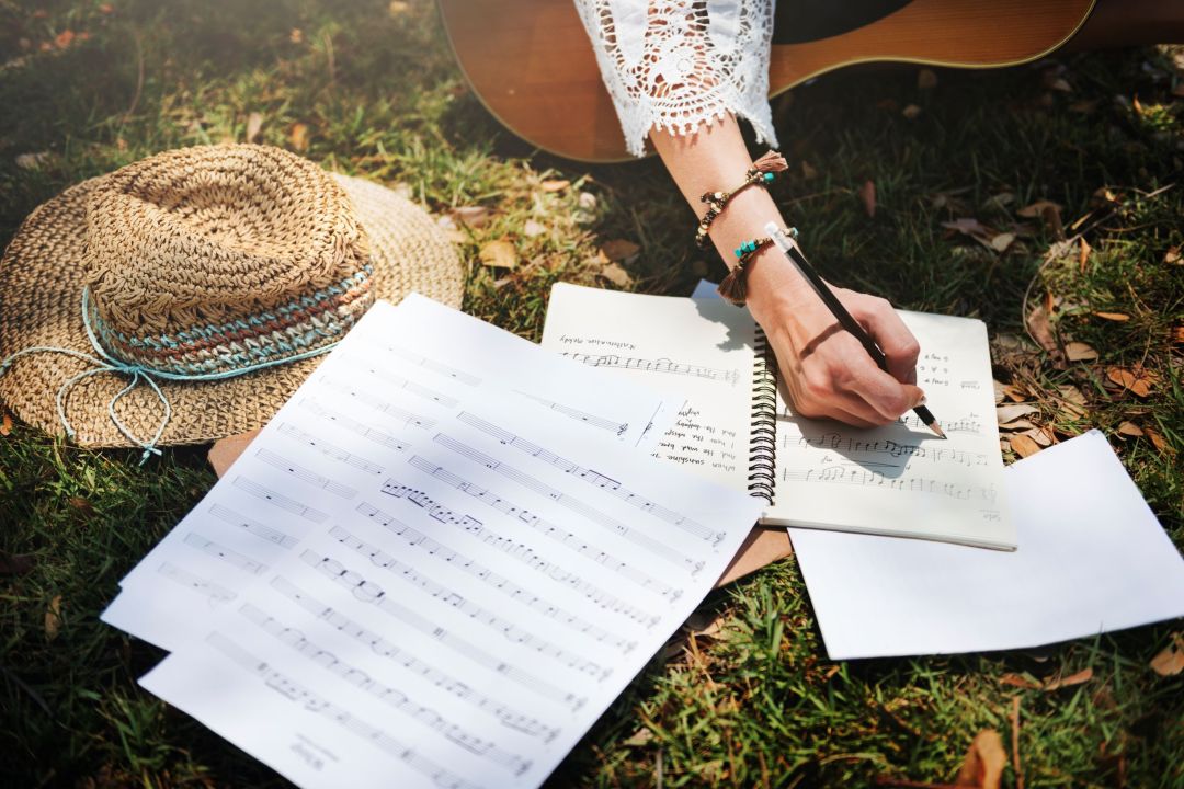 A picture of a woman's arm draped over a guitar as she write music and lyrics, introducing the topic of grammar in English lyrics