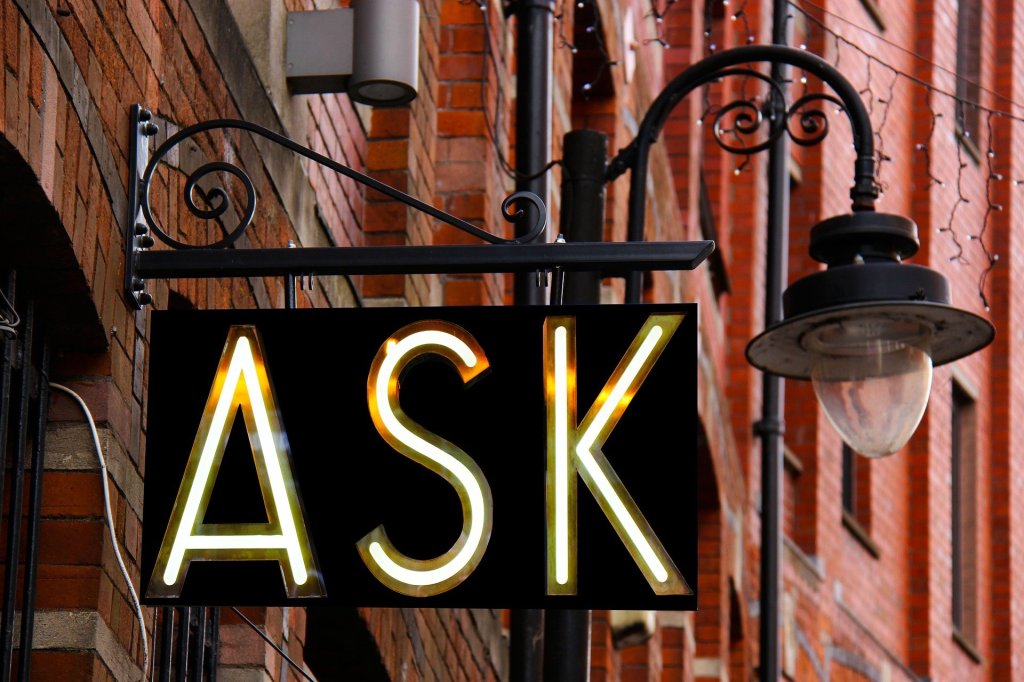 A picture of a wrought iron sign with the word ASK written in illuminated lettering, indicating that clients need to ask for help from me as an English copywriter