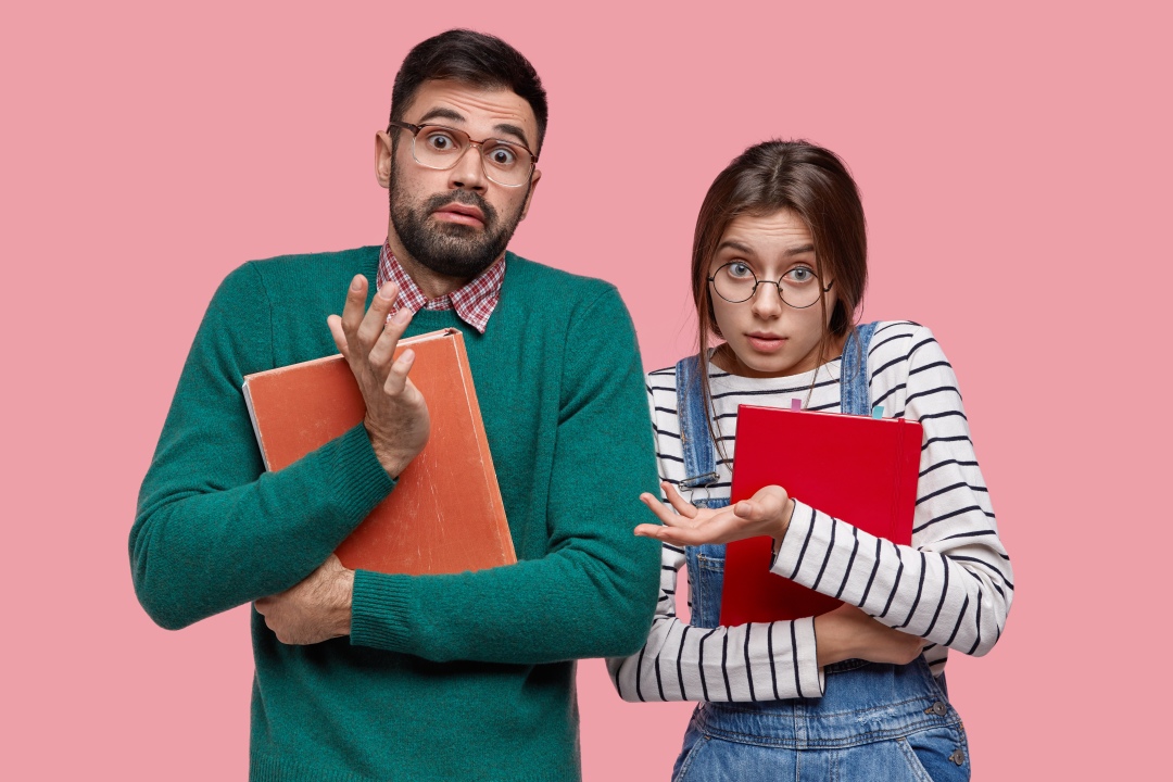 A picture of a man and a woman, each holding a notebook, shrugging their shoulder and confused about whether they need help with English copywriting, English copy editing, or English proofreading