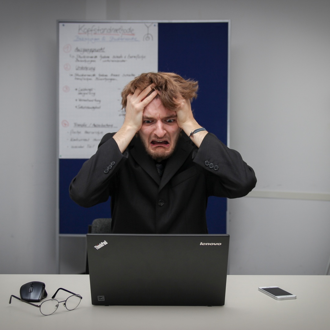 A picture of man with his head in his hands, looking distraught as he stares at his laptop screen.