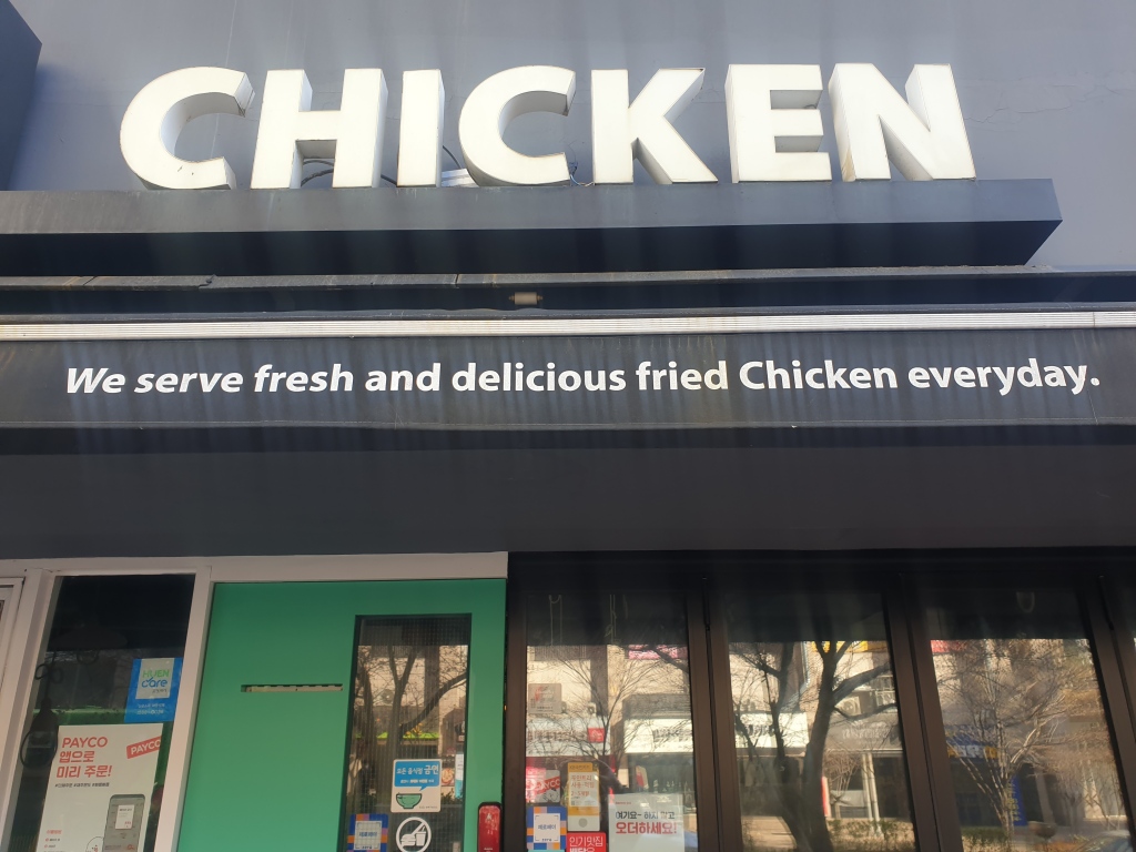 Sign on the awning of a chicken restaurant that reads We serve fresh and delicious fried chicken everyday (everyday is written as one word)